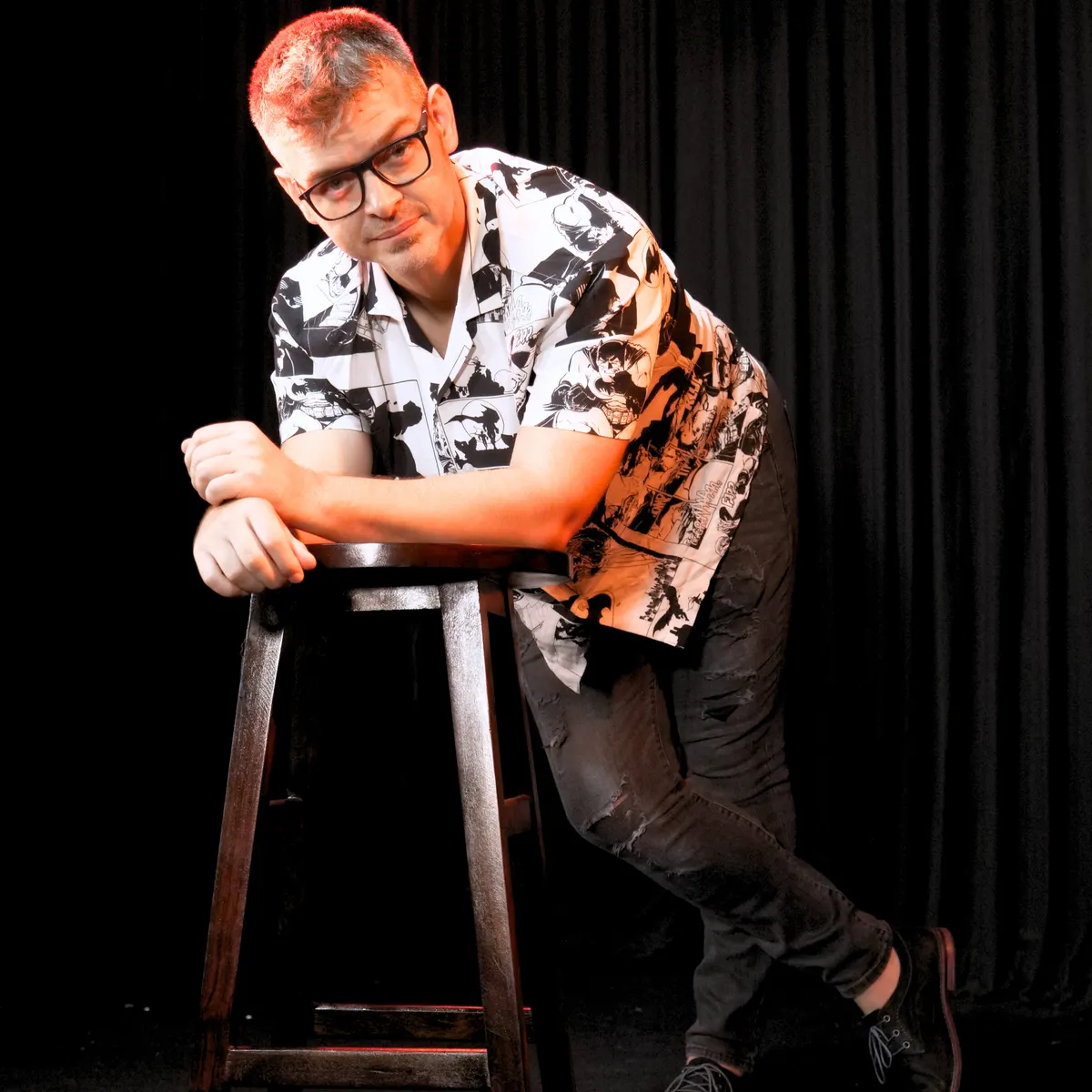 Alex Diaz leaning on a bar stool against red-lit curtains