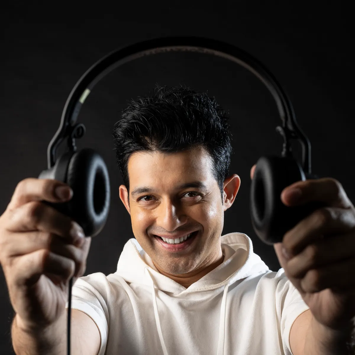 DJ Martin Dsouza offering his headphones to the camera, grinning