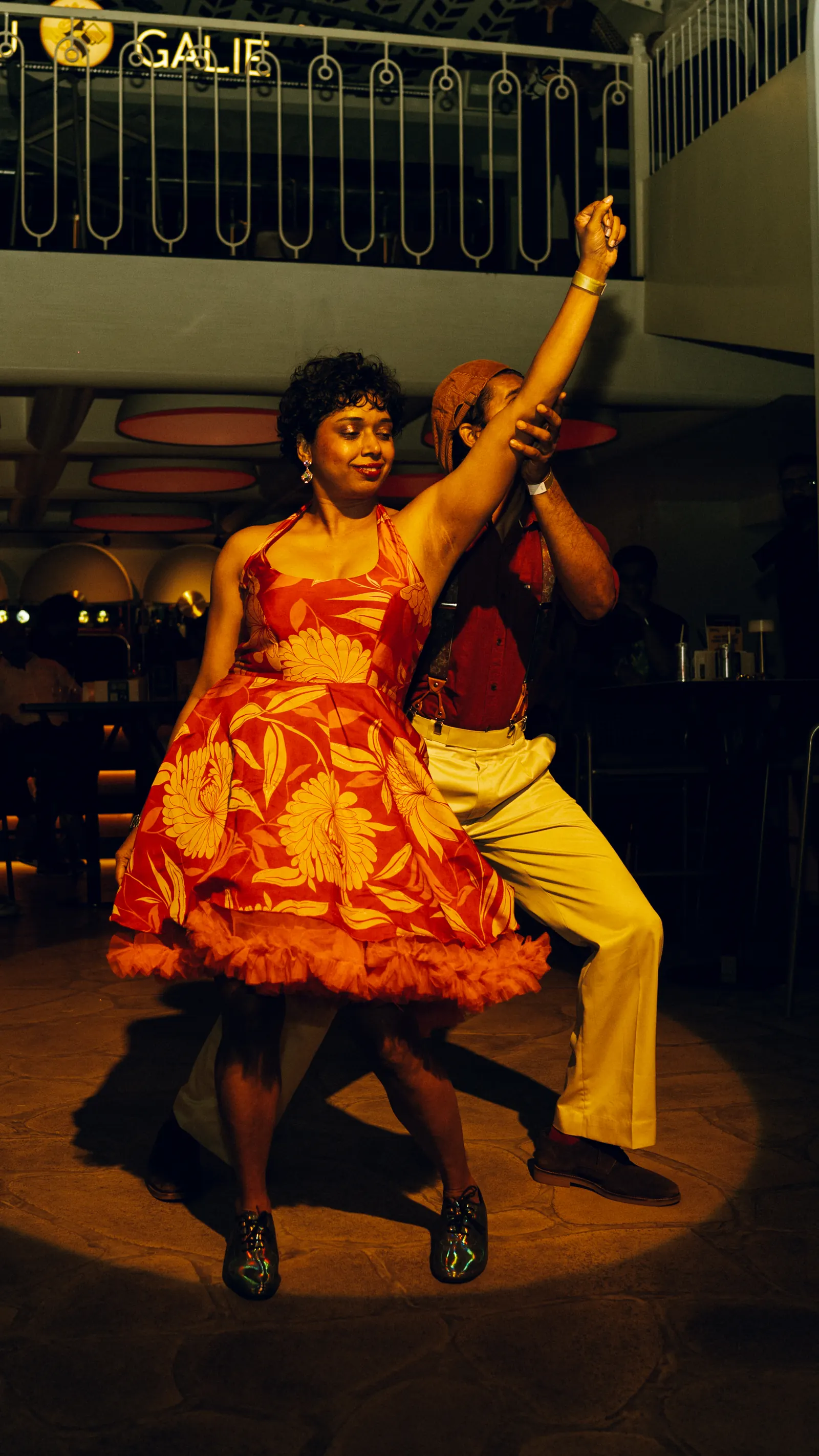 Two performers in a lift, spotlit, the balcony crowd above